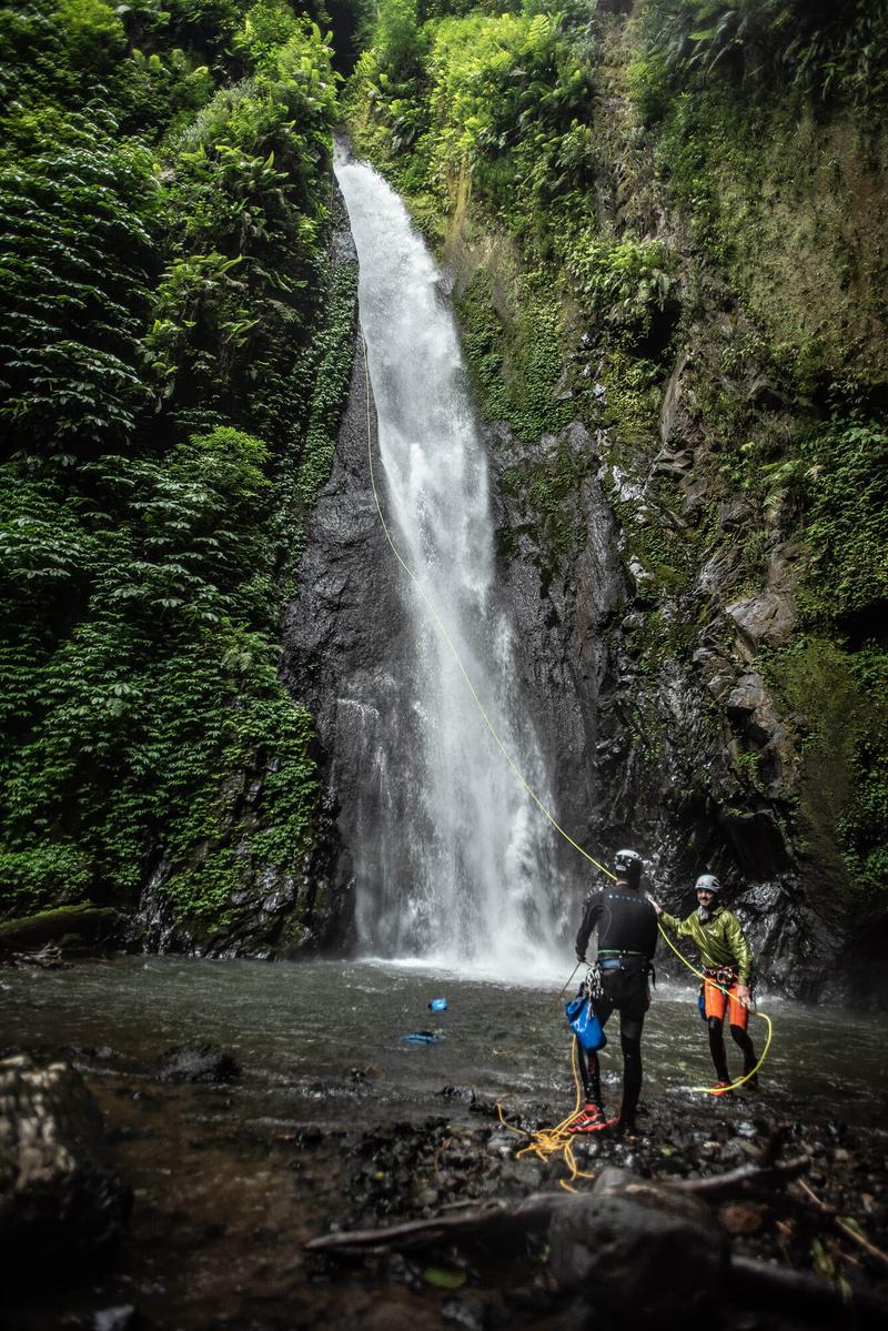 2 canyoneers retrieve a rope down from a beautiful waterfall.